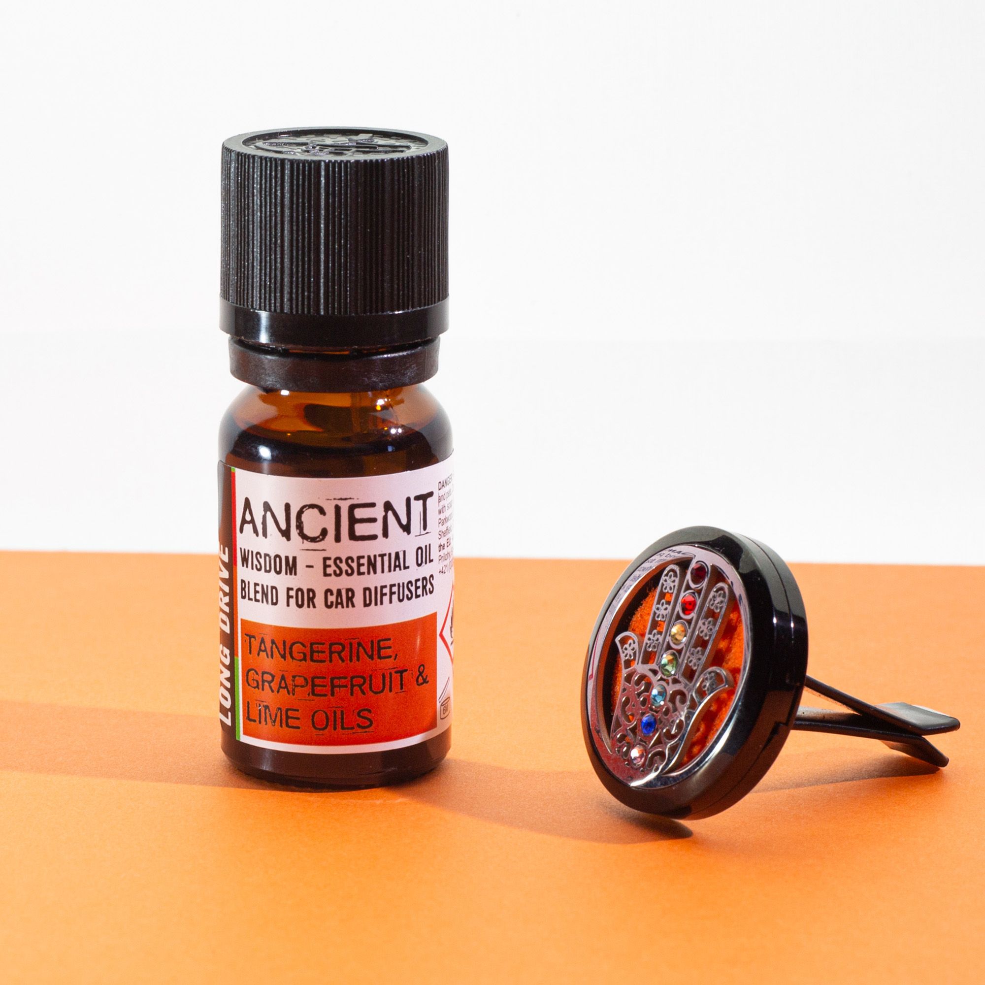 Frasco de mezcla para difusor de coche con mandarina, pomelo y lima junto a un difusor circular sobre fondo naranja.