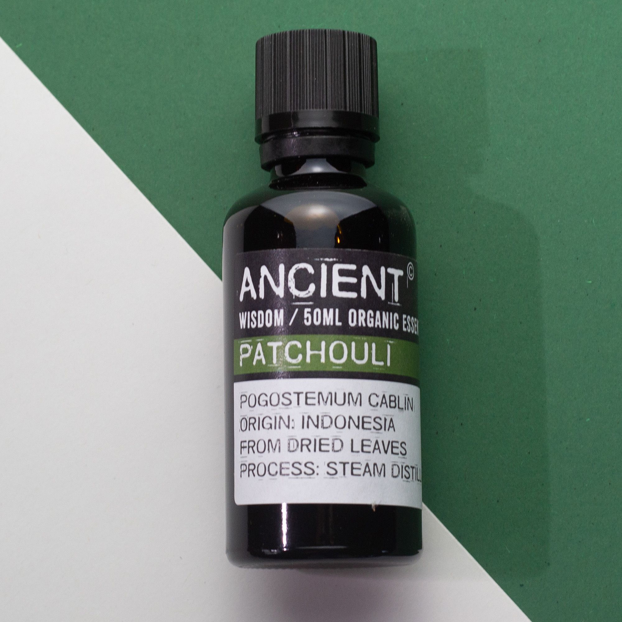 Frasco de aceite esencial orgánico de patchouli 50 ml sobre fondo blanco y verde.