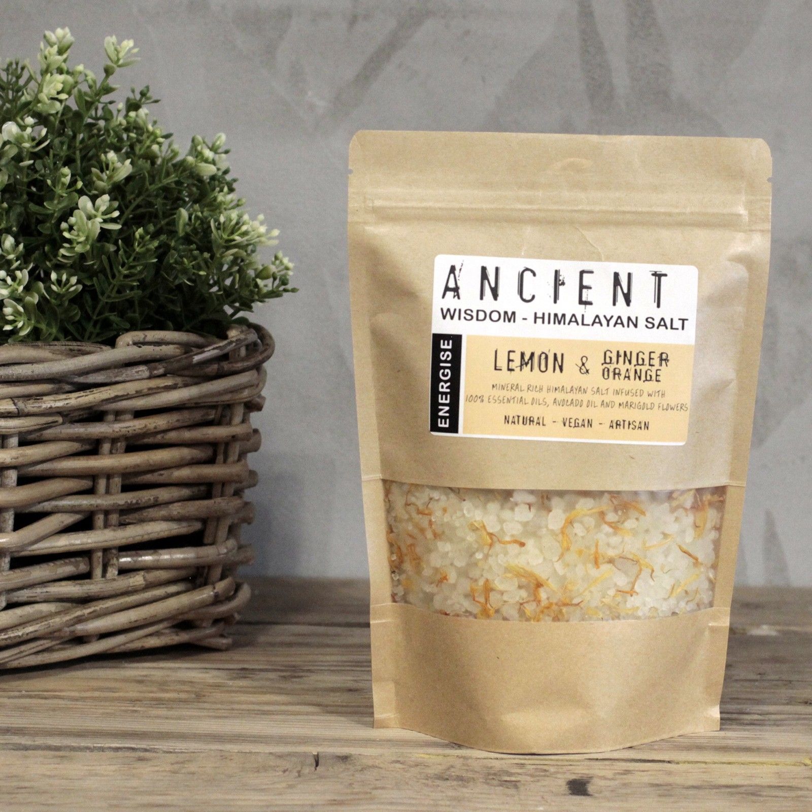 Bolsa de sales de baño del Himalaya Energizar sobre una mesa de madera junto a una cesta con plantas.