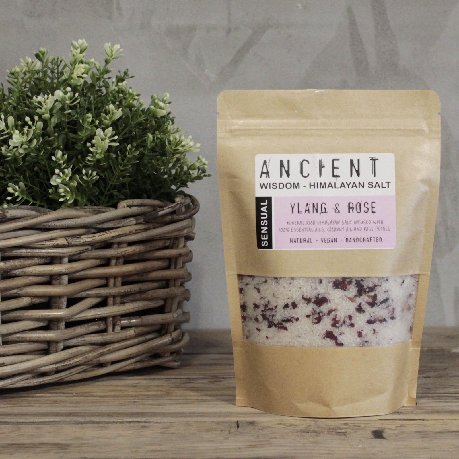 Bolsa de sales de baño del Himalaya Sensual sobre una mesa de madera junto a una cesta con plantas.