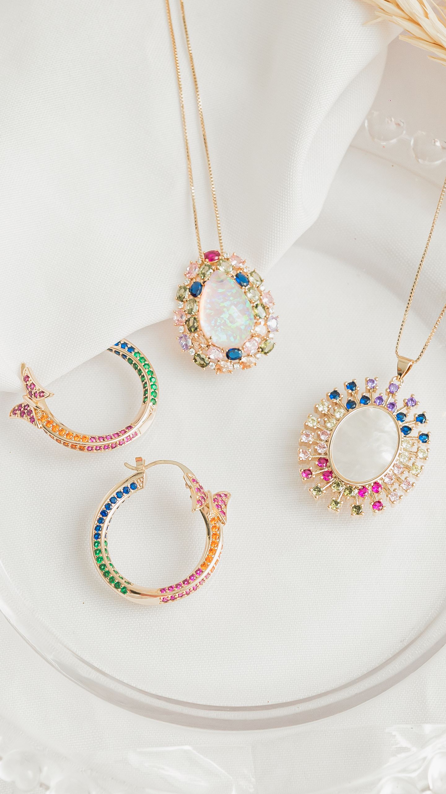 Sofisticadas joyas con piedras preciosas, incluidos colgantes y pendientes, exhibidas sobre tela blanca.